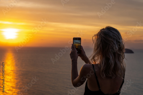 Fotografia Woman hands holding mobile phone at sunset