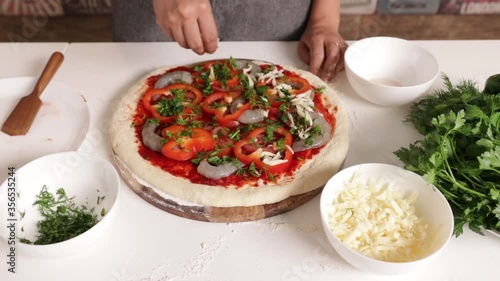 chef prepares pizza with shrimps. the chef's hands sprinkle parmesan on the prepared crust with tomatoes, shrimps, herbs and mozzarella. without face.