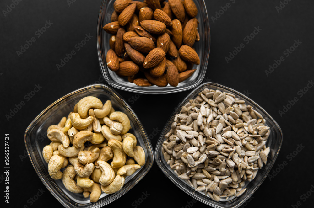 Almond, cashew and sunflower seeds in a small plates which standing on a black table. Nuts is a healthy vegetarian protein and nutritious food. Almond, cashew and sunflower seeds in a small plates which standing on a black table. Nuts is a healthy vegetarian protein and nutritious food.