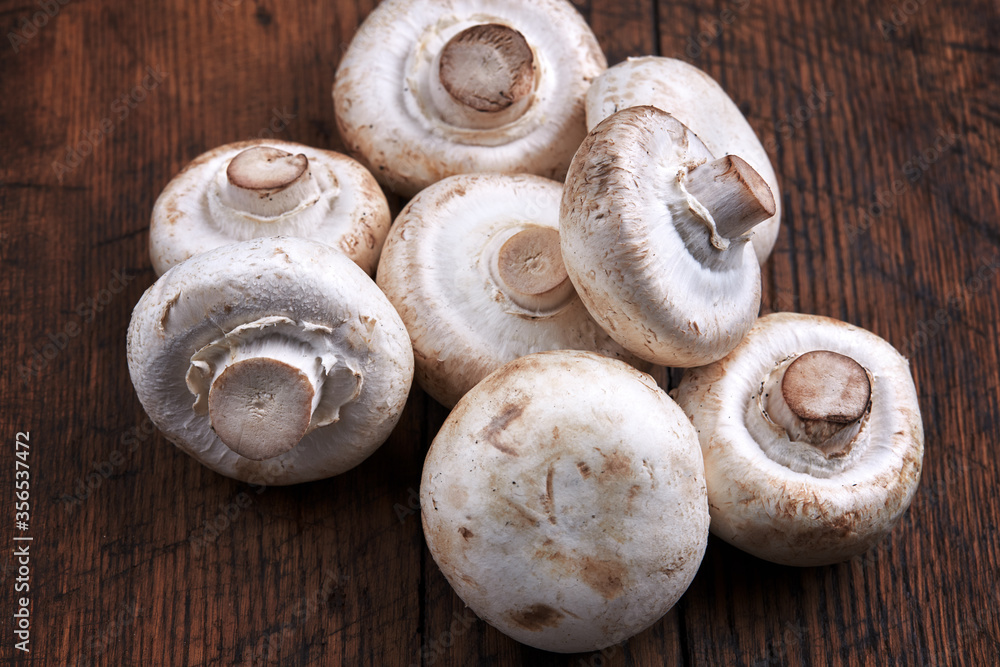 stack of raw fresh champignon mushrooms close up on a wooden rustic background. stack of raw fresh champignon mushrooms close up on a wooden rustic background.