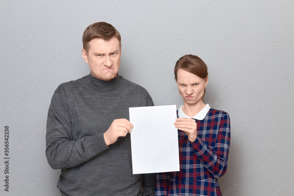 Portrait of adult couple holding together white blank paper sheet Portrait of adult couple holding together white blank paper sheet