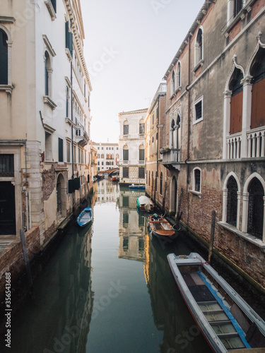Still canal with reflections of houses and boats in Venice, Italy at sunrise in summer © Alexx