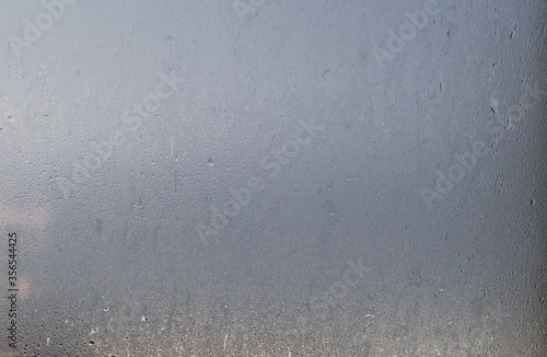 Morning rain drops on a glass window with blurred blue sky background, view through a wet and sweaty window with a cope and text space
