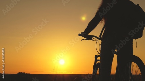 Free girl travels with bicycle at sunset. concept of adventure and travel. Hiker healthy young woman rides bicycle to edge of hill  enjoying nature and sun. lonely woman cyclist resting in park.