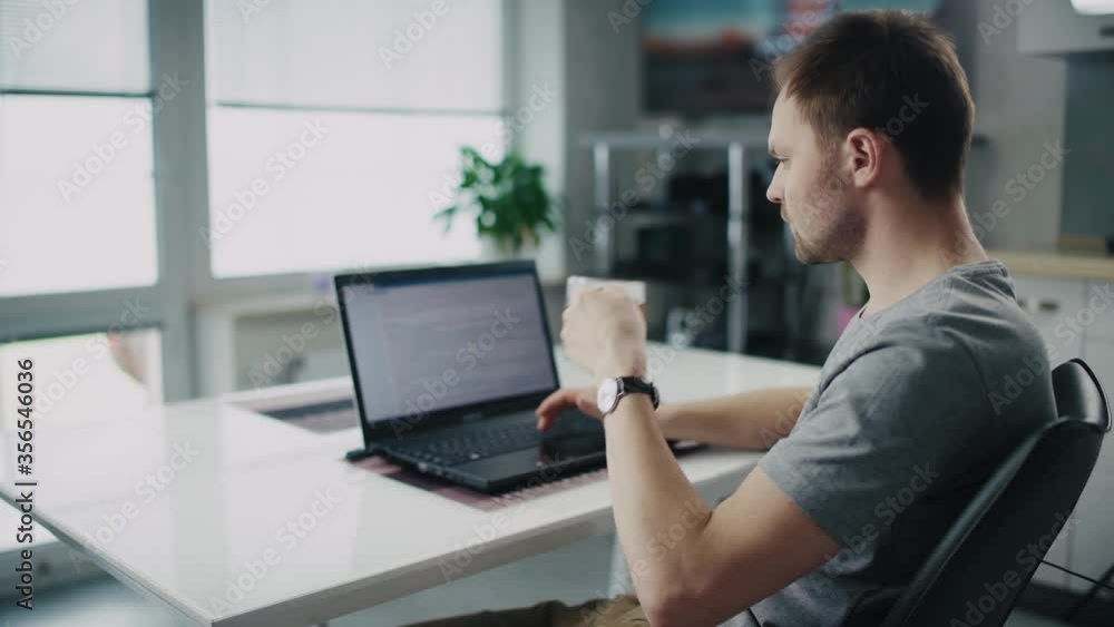 A man is working on a laptop in the kitchen at home. Business at home. Self quarantine, coronavirus, work from home concept. A man is working on a laptop in the kitchen at home. Business at home. Self quarantine, coronavirus, work from home concept.