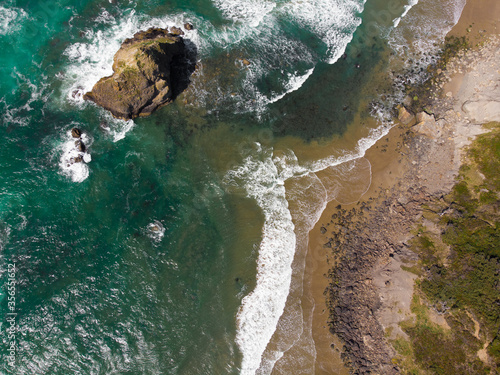 cliff in the pacific ocean with waves, beach and promenade, filmed from a height