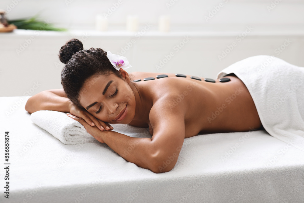 Obraz premium African girl lying at spa salon, getting hot stone massage