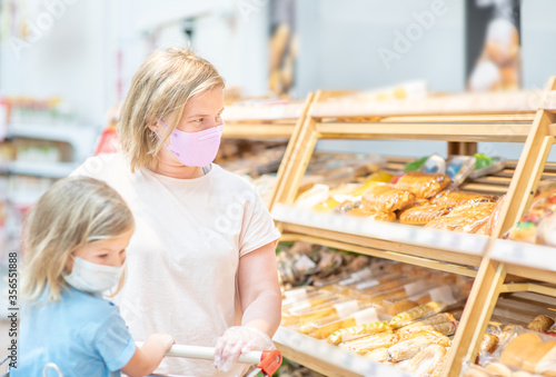 Mother and her little daughter wearing protective face mask shop at a supermarket during the coronavirus epidemic or flu outbreak