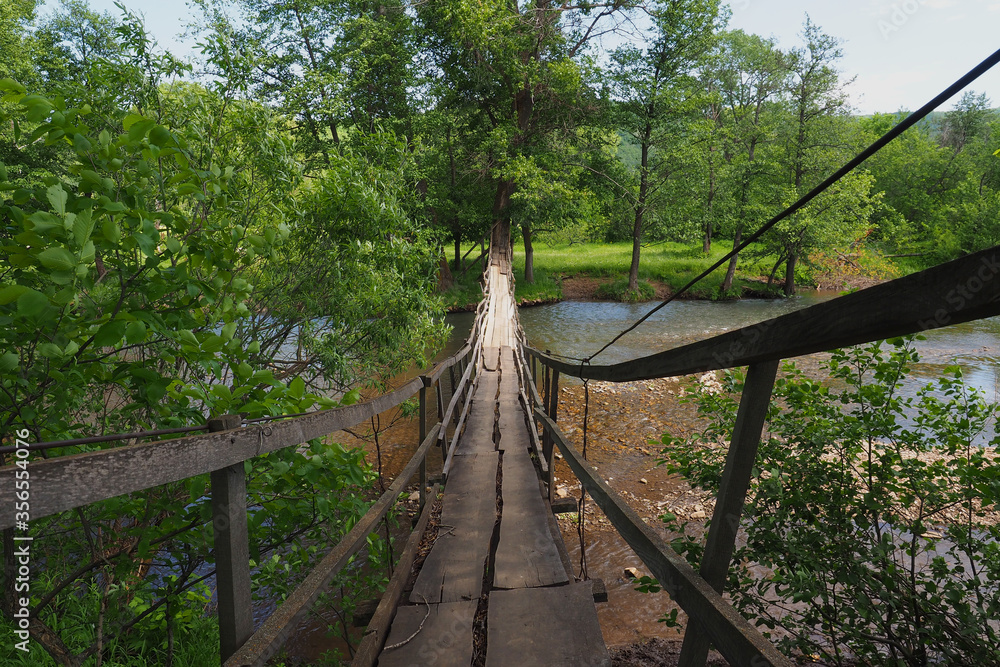 Wooden suspension bridge over a small river flowing in the forest. Summer landscape. Wooden suspension bridge over a small river flowing in the forest. Summer landscape.