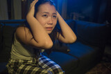 young beautiful sad and depressed Asian Korean woman crying in tears on darkness in pain feeling worried and helpless sobbing desperate at living room sofa couch