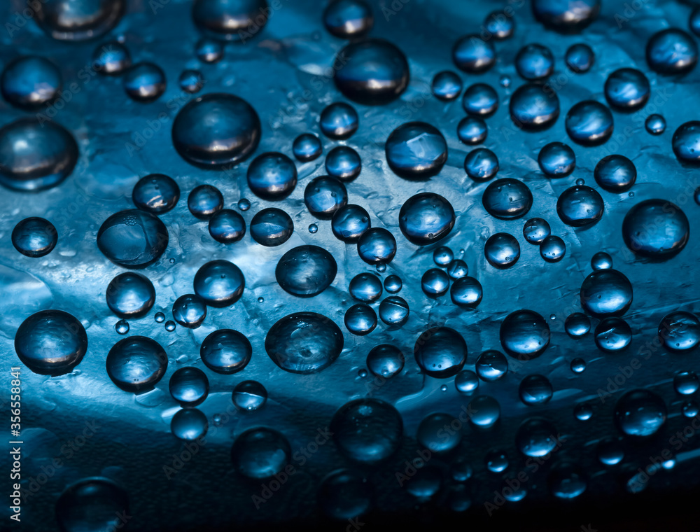Abstract deep blue background of drops and droplets. Close up. Illuminated by the bright sun blue drops of water are falling down.