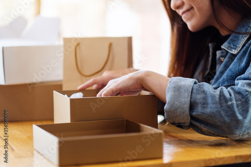 A beautiful young asian woman receiving and opening a postal parcel box at home for delivery and online shopping concept