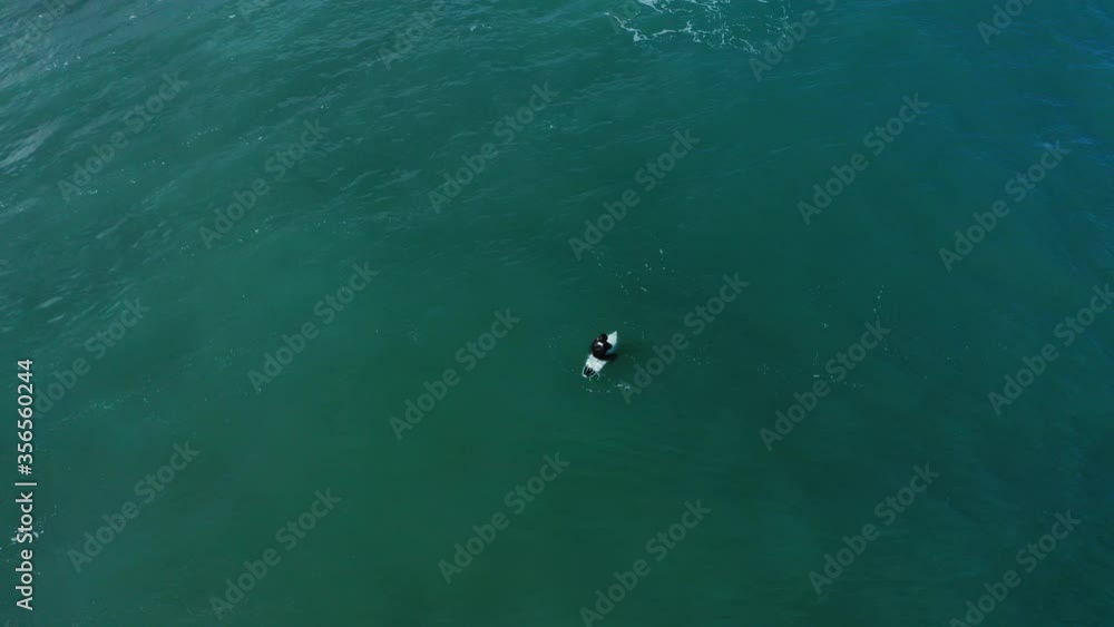 Surfer using a wetsuit sitting on his surfboard and waiting alone for the perfect wave. Surfer using a wetsuit sitting on his surfboard and waiting alone for the perfect wave.