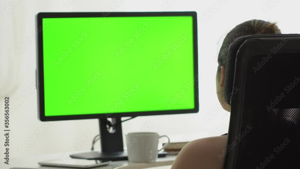 Young woman is Sitting on a office chair and Watching monitor with Horizontal Green Screen Mock Up. Young woman is Sitting on a office chair and Watching monitor with Horizontal Green Screen Mock Up.