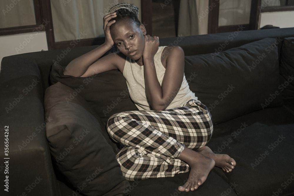 Obraz premium young Afro American woman suffering depression - sad and depressed black teenager girl in pain at home sofa couch feeling overwhelmed and emotional crying lonely in the dark