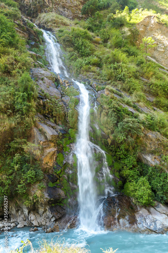 A waterfall spotted in Tal, Annapurna Circuit Trek, Nepal. Few hundred meters of free fall, waterfall surrounded by tall mountains slopes, covered with green bushes and trees. Smooth capture