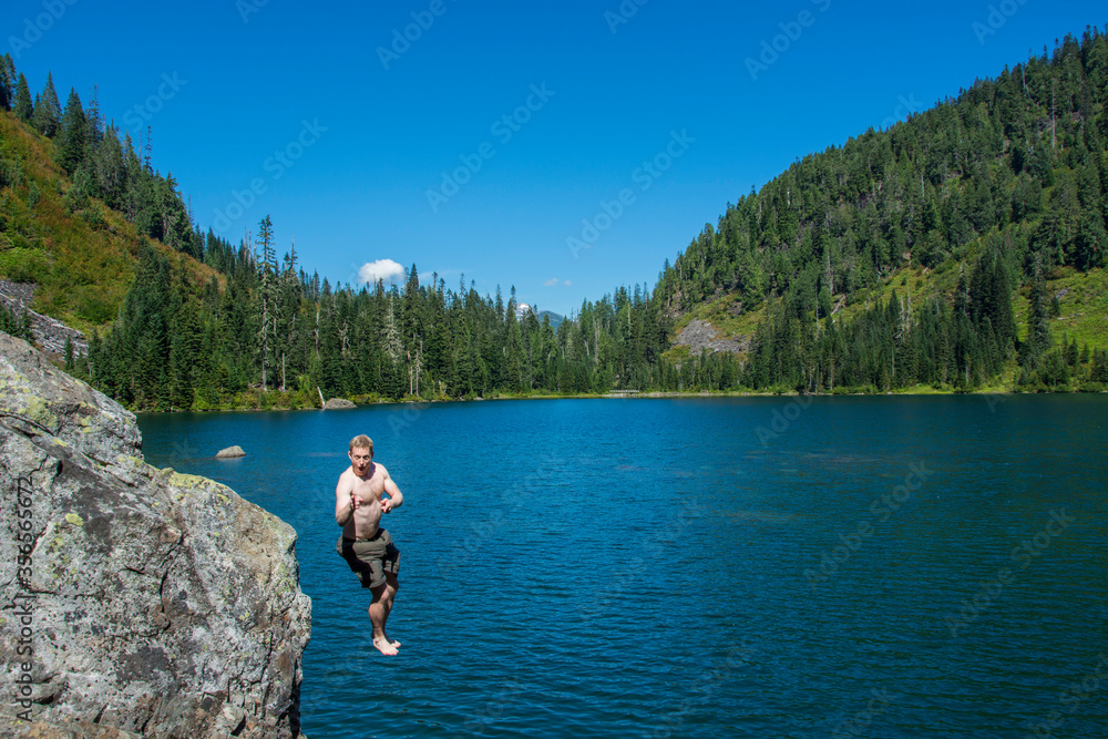 Adventurous male hiker jumping into an alpine lake in Washington State.