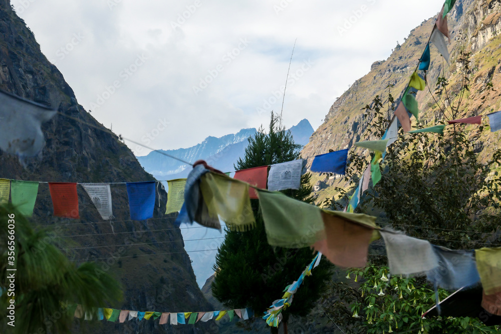 A few lines of prayer flags waving on the wind in Himalayan village, Tal, Nepal, along Annapurna Circuit Trek. There are high mountain chain around. Spirituality and meditation.
