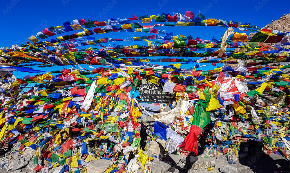 The waving flags at the top of Thorung La Pass, Annapurna Circuit Trek Nepal. Congratulations for the effort. Colorful prayer flags attached to the stone wall, blow by the wind. Clear sky. Achievement