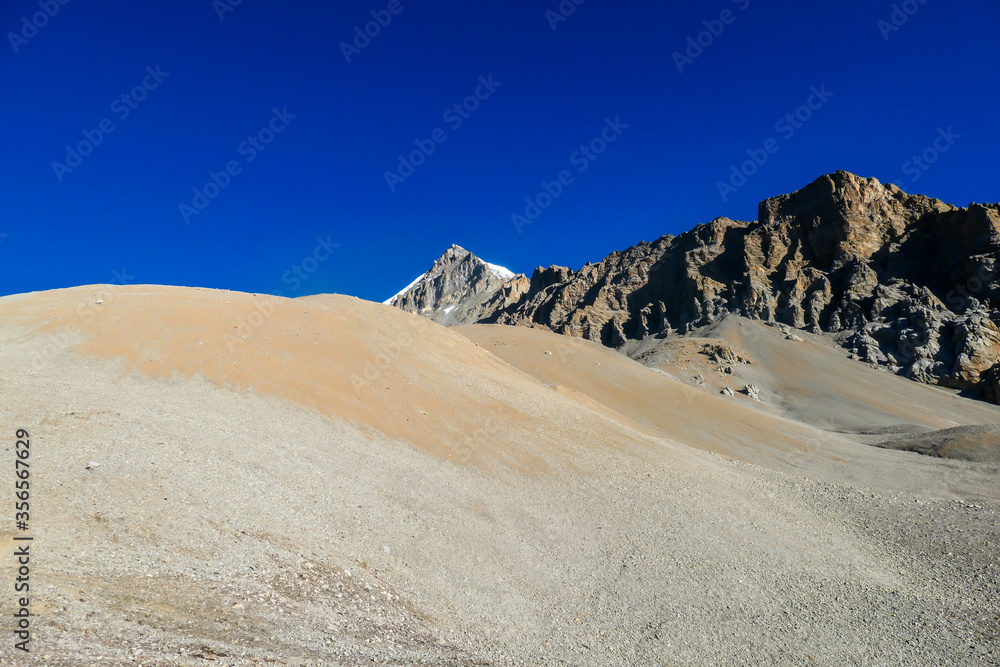 An idyllic landscape of Himalayas in the nearby of Thorung La Pass, Annapurna Circuit Trek, Nepal. Harsh and barren landscape around. Clear and blue sky. Snow capped mountains. Early morning