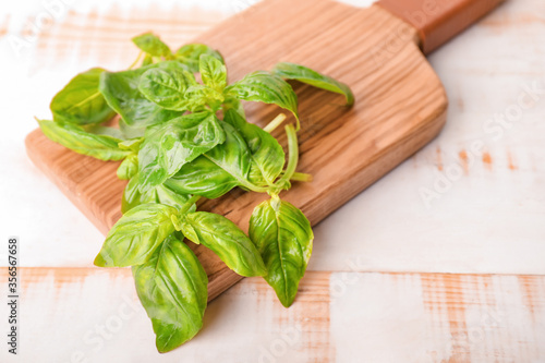 Cutting board and fresh green basil on wooden background