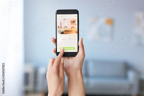 Young woman with mobile phone booking room in hotel online at home