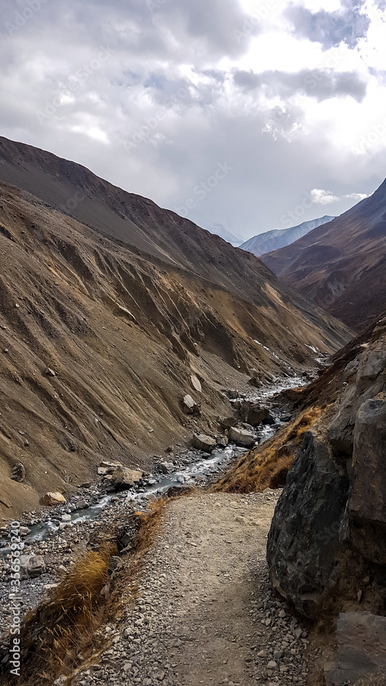 A small torrent flowing in Manang Valley, Annapurna Circus Trek, Himalayas, Nepal, with the view on Annapurna Chain. Dry and desolated landscape. High, snow capped mountain peaks.