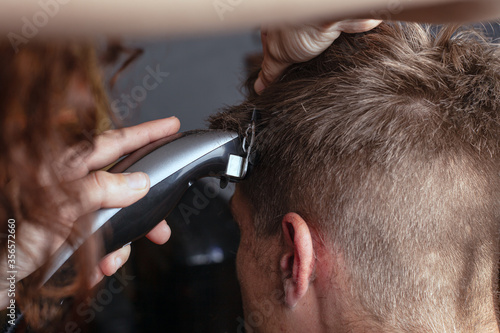 girl cuts a man with a hair trimmer, hairdresser