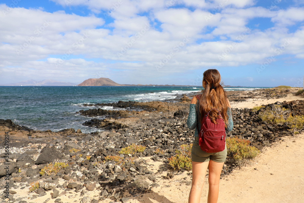 Rear view of young female backpacker hiking looks on the sea in Fuerteventura Island, Spain