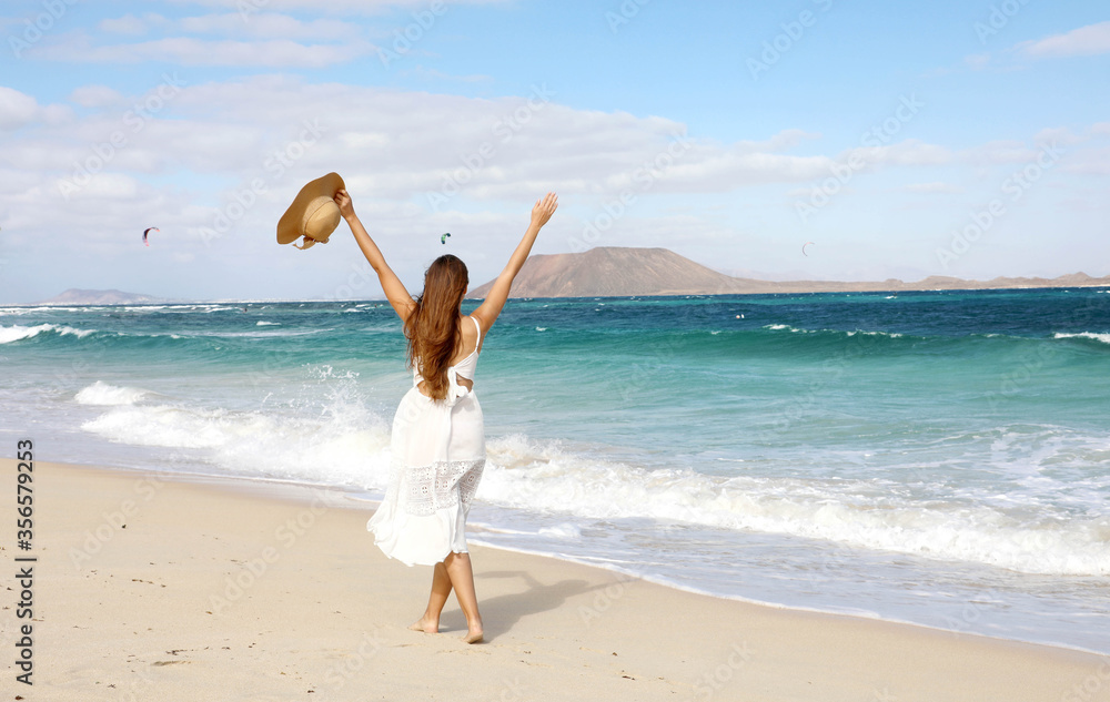 Freedom happy girl enjoying wind with raised arms and people kitesurfering, Corralejo Dunes beach, Fuerteventura, Canary Islands Freedom happy girl enjoying wind with raised arms and people kitesurfering, Corralejo Dunes beach, Fuerteventura, Canary Islands