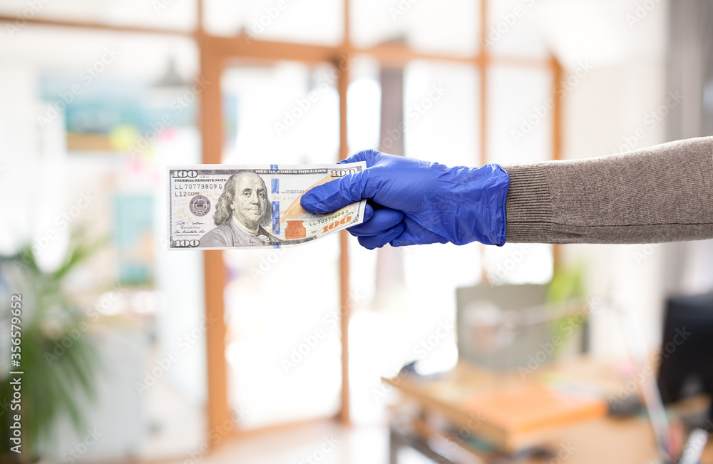 finance, bank and hygiene concept - close up of hand in medical glove with money over office background