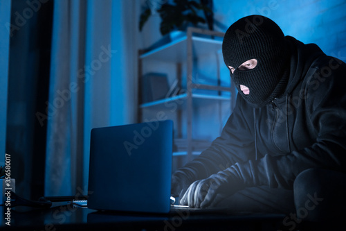 Plakat Masked hacker downloading private information using pc