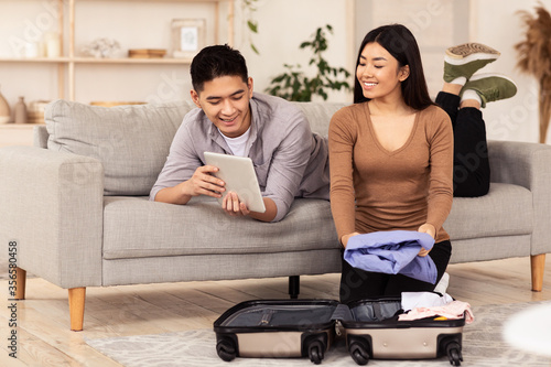 Asian Couple Using Tablet Packing For Vacation Sitting At Home