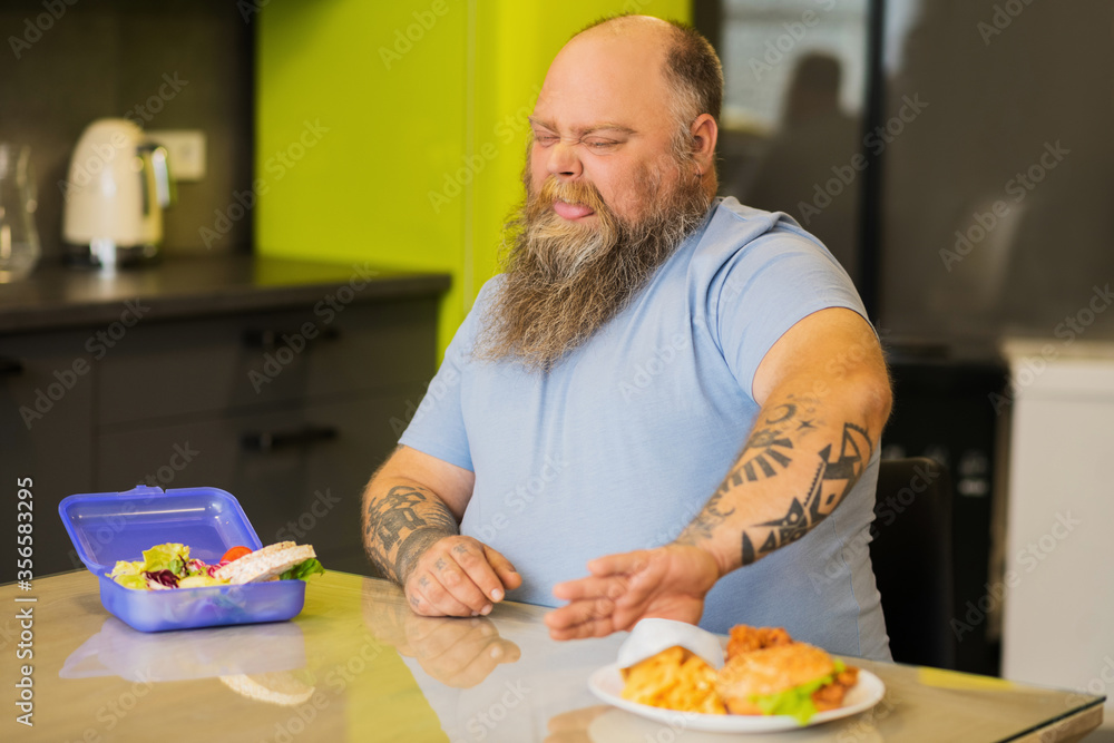 Fat man with grimace pushing away fast food
