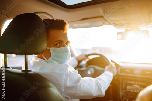 Man driving a car puts on a medical mask during an epidemic in quarantine city. Health protection, safety and pandemic concept. Covid- 19.