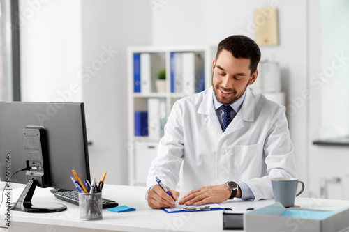 healthcare, medicine and people concept - smiling male doctor with clipboard at hospital