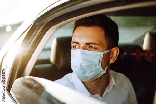 Man passenger in protective sterile medical mask in the taxi car during an epidemic in quarantine city. Health protection, safety and pandemic concept. Covid - 19.

