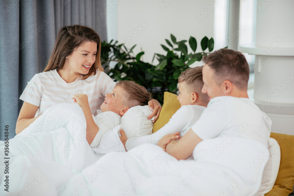 Fototapeta premium Young family enjoying at home. Happy parents with sons relaxing on sofa. 