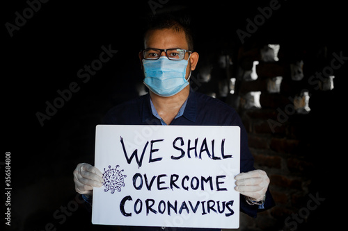 A young man wearing a medical mask and safety gloves stands with a placard message to 