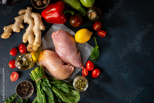 Chicken meat and fresh vegetables top view on dark background