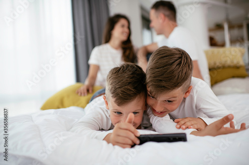 Two little brothers are playing games on the phone. Beautiful boys enjoying at home.