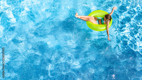 Active young girl in swimming pool aerial top view from above, child relaxes and swims on inflatable ring donut and has fun in water on family vacation, tropical holiday resort 