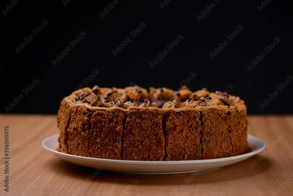 Delicious nut cake glazed with dark chocolate icing served on a white plate on light wooden table background. Delicious nut cake glazed with dark chocolate icing served on a white plate on light wooden table background.
