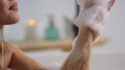 Closeup unrecognized woman washing hands in bathroom. Girl blowing foam in bath.