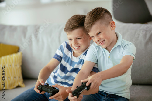 Happy brothers playing video games. Young brothers having fun while playing video games in living room	
