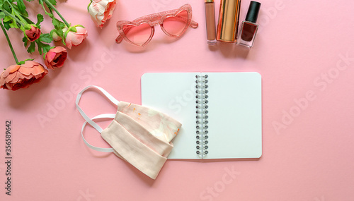 Flat lay of blogger concept during corona virus. Open empty notebook with mask, glasses, and feminine accessories on the pink background.
