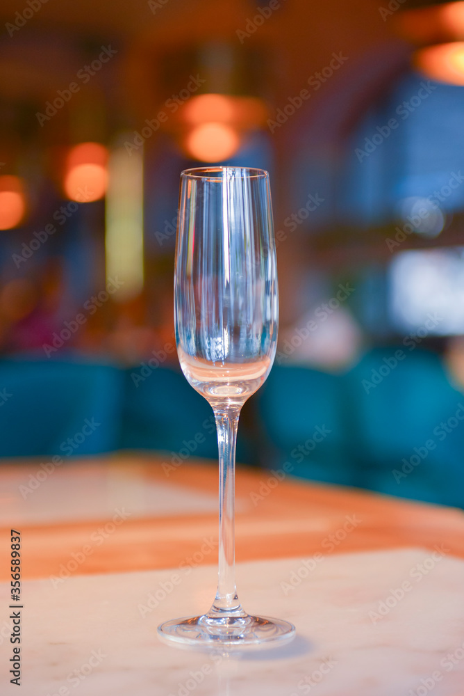 Transparent empty champagne glass on the rustic wooden table over blurred restaurant background. Transparent empty champagne glass on the rustic wooden table over blurred restaurant background.