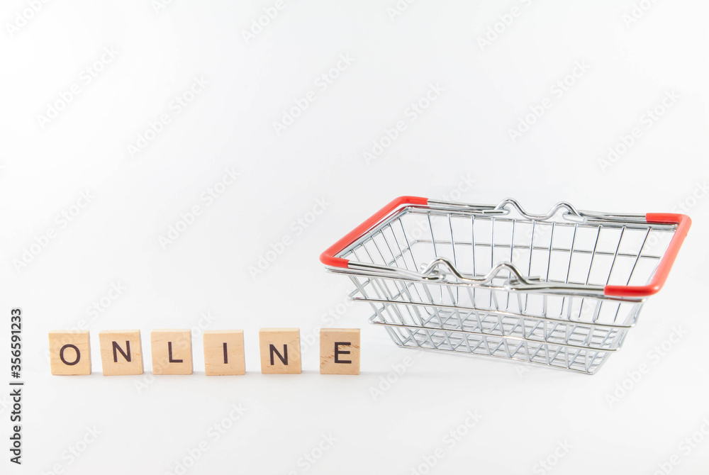 Online shopping. Square metal shopping basket with red handles with wooden alphabet block on white background with copy space. Concept of e-commerce during coronavirus pandemic crisis.