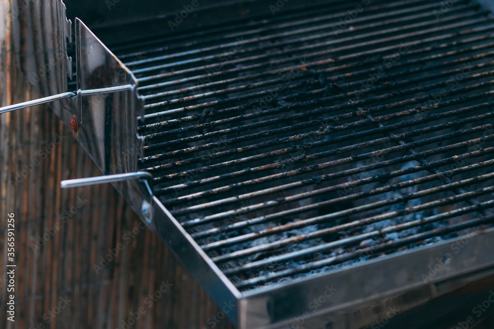 Fototapeta premium Part of dirty Barbecue Grill Grate after cooking. Empty grill grate. Side view of a barbecue grill grate with lava stones beneath it, lit by sunlight. Cooking on the balcony. Meat cooking device