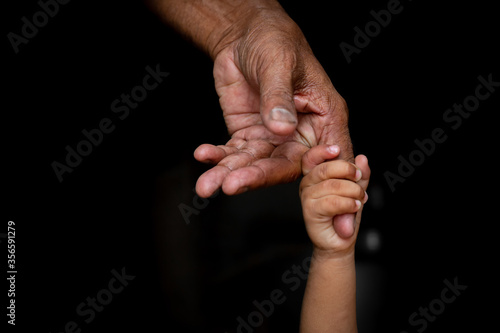 A baby's hands holding tightly A senior man's old age finger. Family, Generation, Support and people concept. Dark background.